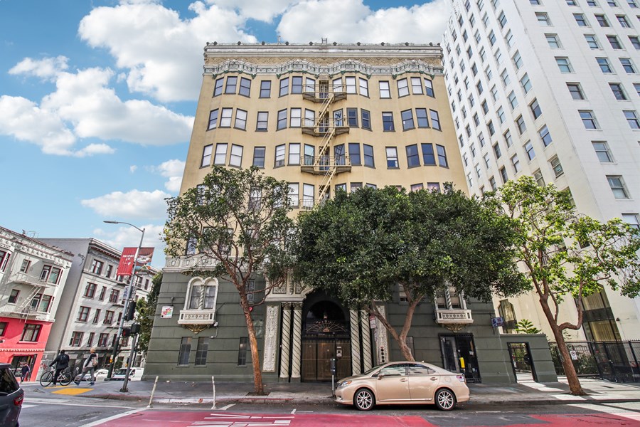 A car is parked in front of a building with a tree in front of it.